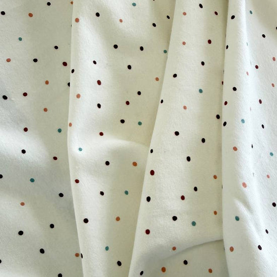 White cotton jersey knit fabric with small multicolor dot print and soft stretch texture.