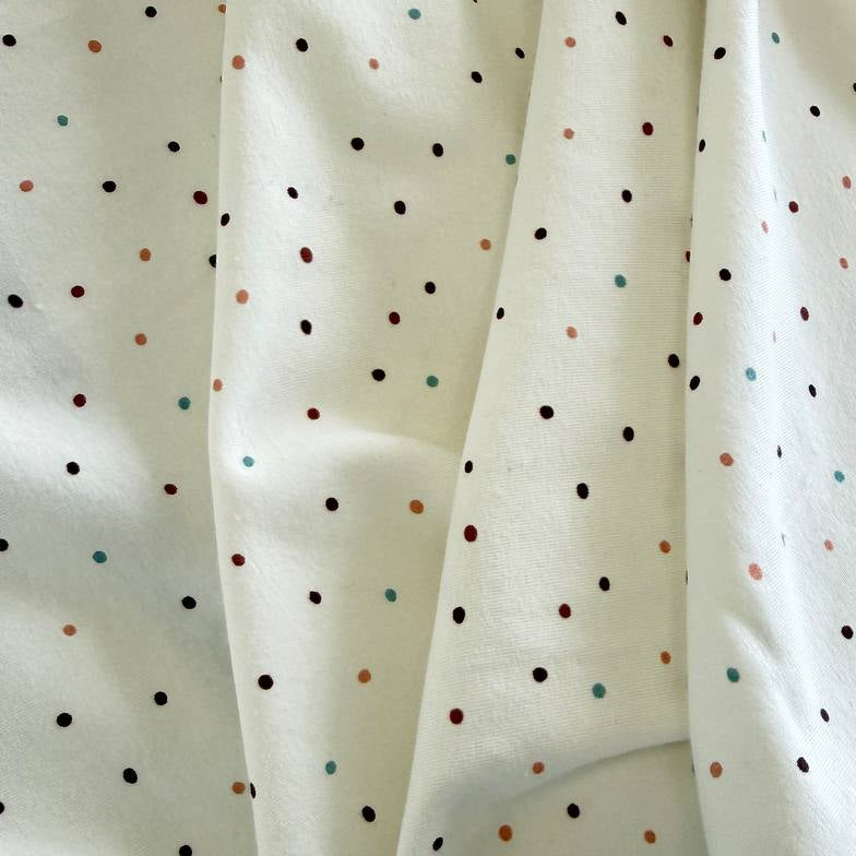 White cotton jersey knit fabric with small multicolor dot print and soft stretch texture.