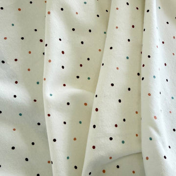 White cotton jersey knit fabric with small multicolor dot print and soft stretch texture.