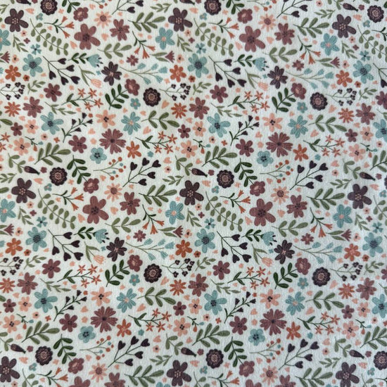 Noote floral cotton jersey fabric with dusty pink, mauve, sage, and blue flowers on an ivory background.