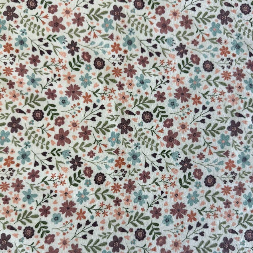 Noote floral cotton jersey fabric with dusty pink, mauve, sage, and blue flowers on an ivory background.