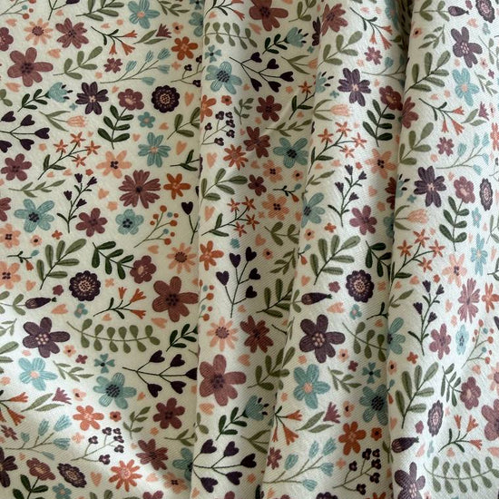 Noote floral cotton jersey fabric with dusty pink, mauve, sage, and blue flowers on an ivory background.