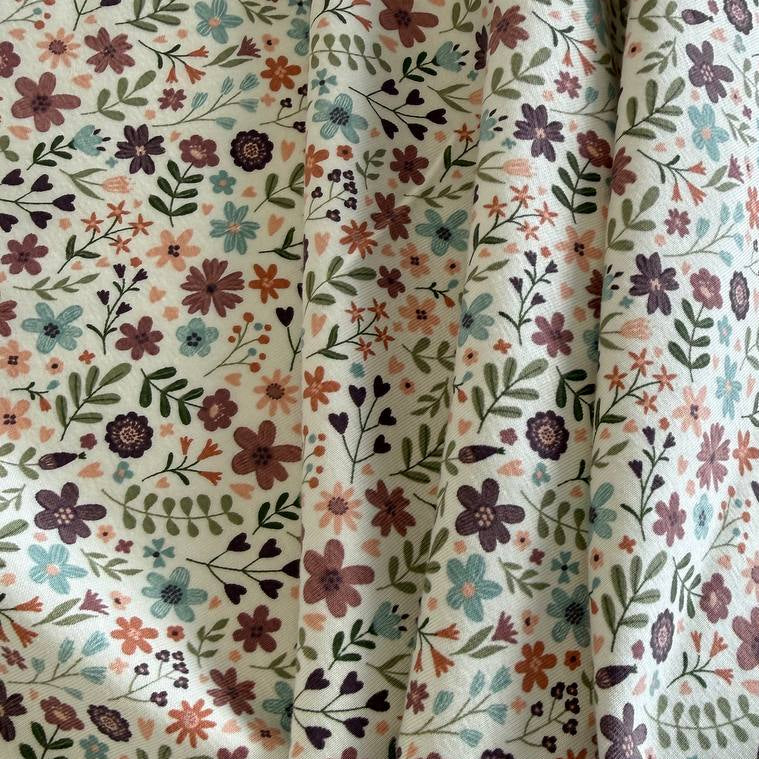 Noote floral cotton jersey fabric with dusty pink, mauve, sage, and blue flowers on an ivory background.