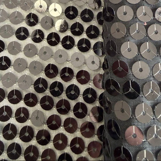 Black sequin fabric with dense round sequins sewn onto a soft mesh base, creating a bold reflective surface and fluid drape.