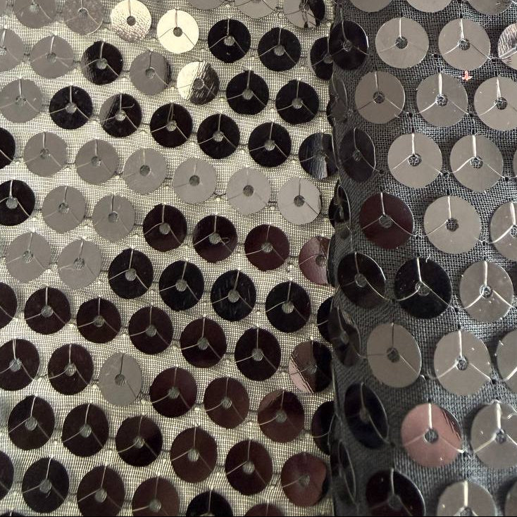 Black sequin fabric with dense round sequins sewn onto a soft mesh base, creating a bold reflective surface and fluid drape.