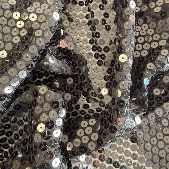 Black sequin fabric with dense round sequins sewn onto a soft mesh base, creating a bold reflective surface and fluid drape.