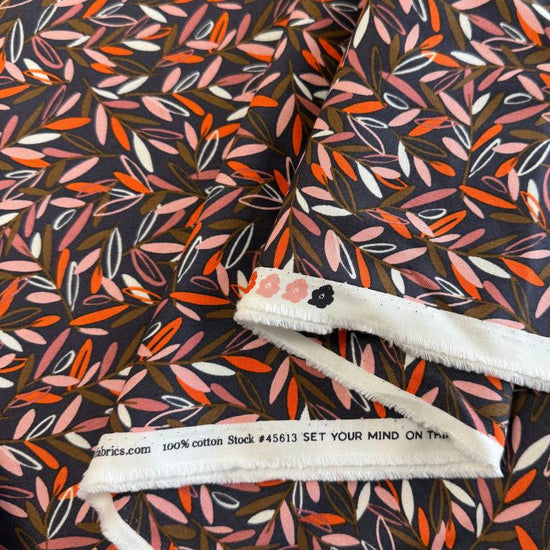 Modern quilting cotton fabric featuring an all-over scattered leaf print in blush pink, orange, cream, and olive tones on a charcoal grey background from the Things Above collection by Fancy That Design House for Moda Fabrics.