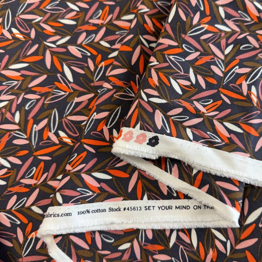 Modern quilting cotton fabric featuring an all-over scattered leaf print in blush pink, orange, cream, and olive tones on a charcoal grey background from the Things Above collection by Fancy That Design House for Moda Fabrics.