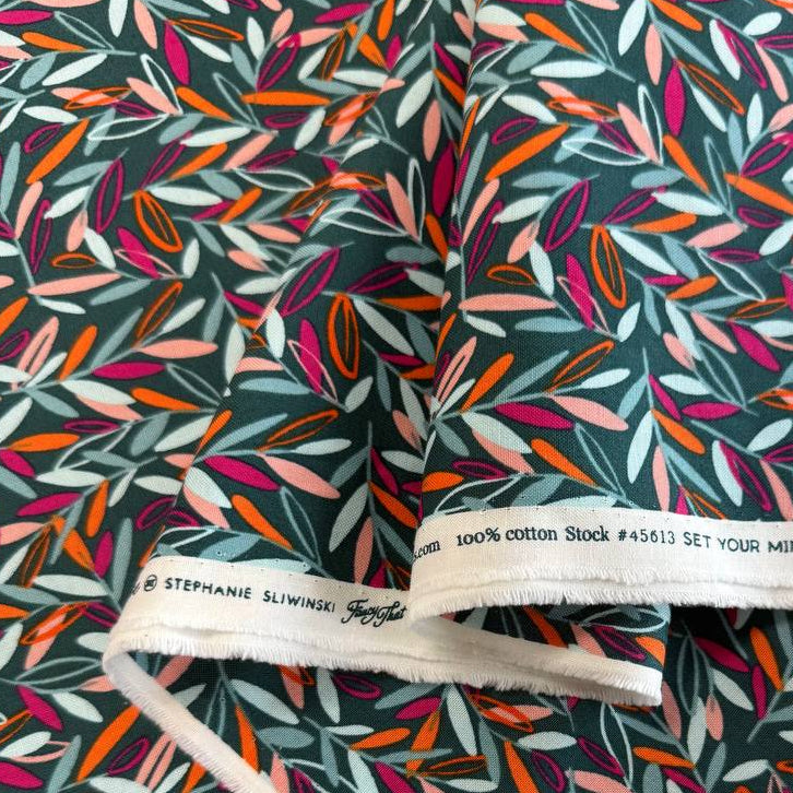 Modern quilting cotton fabric featuring an all-over scattered leaf print in teal, blush pink, orange, aqua, and magenta tones on a deep teal background from the Things Above collection by Fancy That Design House for Moda Fabrics.