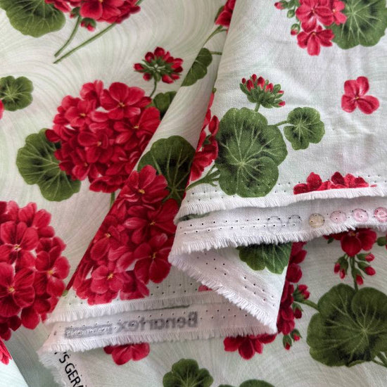 Red geranium flowers and green leaves scattered across a soft mint background quilting cotton fabric from Betty's Geraniums by Jackie Robinson for Benartex.