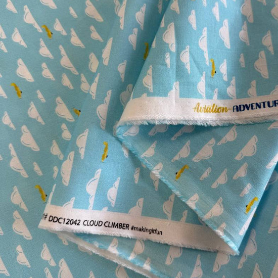 Light sky-blue quilting cotton featuring white clouds and small golden airplanes from the Aviation Adventures collection by Michael Miller.