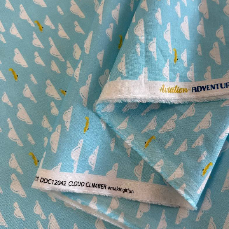Light sky-blue quilting cotton featuring white clouds and small golden airplanes from the Aviation Adventures collection by Michael Miller.