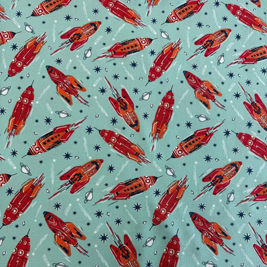 Retro red and orange rockets flying across a light aqua blue background with stars and planets, Blast Off Blue Nebula quilting cotton by Stacy Iest Hsu for Moda Fabrics.