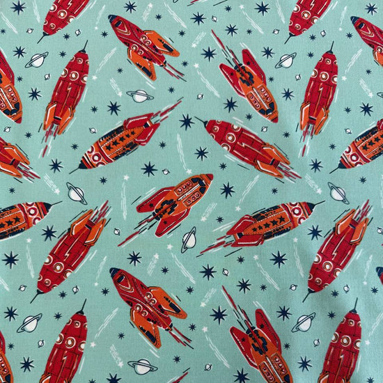 Retro red and orange rockets flying across a light aqua blue background with stars and planets, Blast Off Blue Nebula quilting cotton by Stacy Iest Hsu for Moda Fabrics.