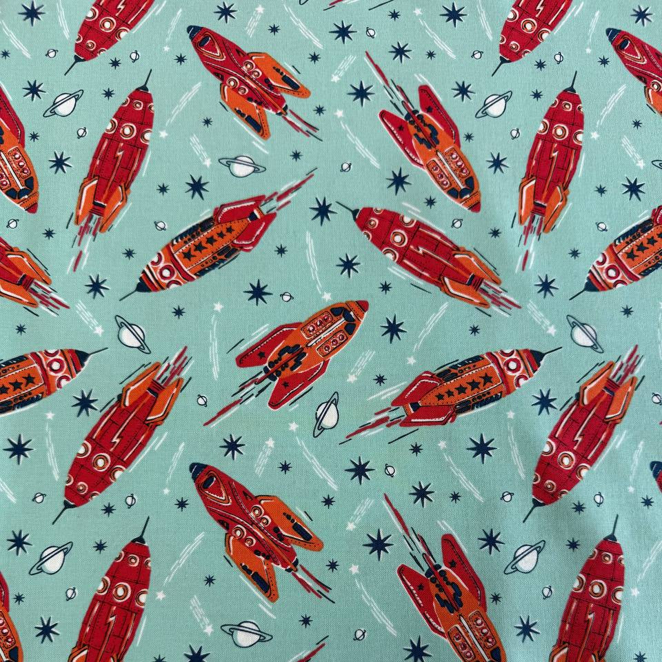 Retro red and orange rockets flying across a light aqua blue background with stars and planets, Blast Off Blue Nebula quilting cotton by Stacy Iest Hsu for Moda Fabrics.