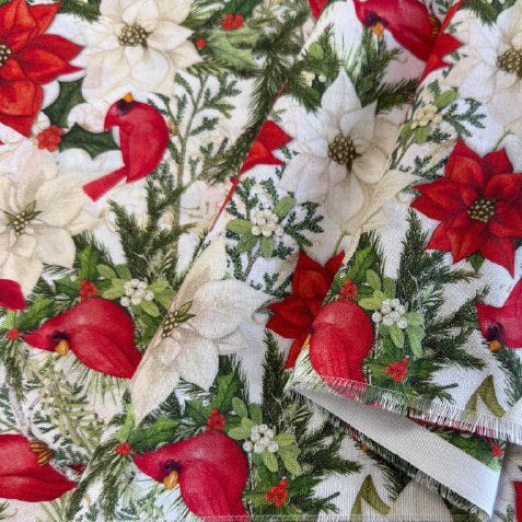 Christmas cotton fabric featuring red cardinals, white and red poinsettias, evergreen branches, and holiday greenery on a white background.