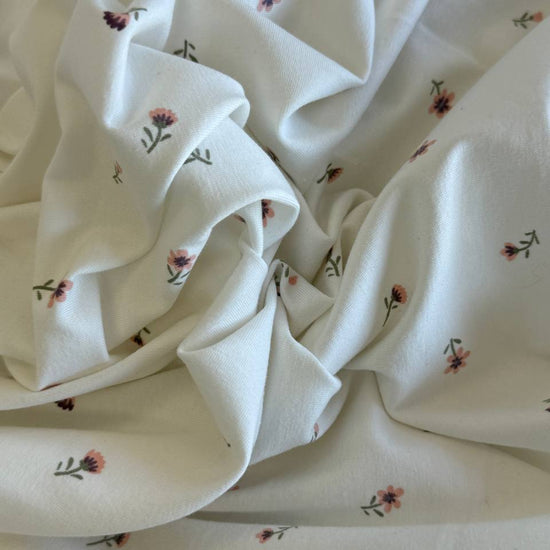 Floral cotton jersey knit fabric with small pink flowers on cream background