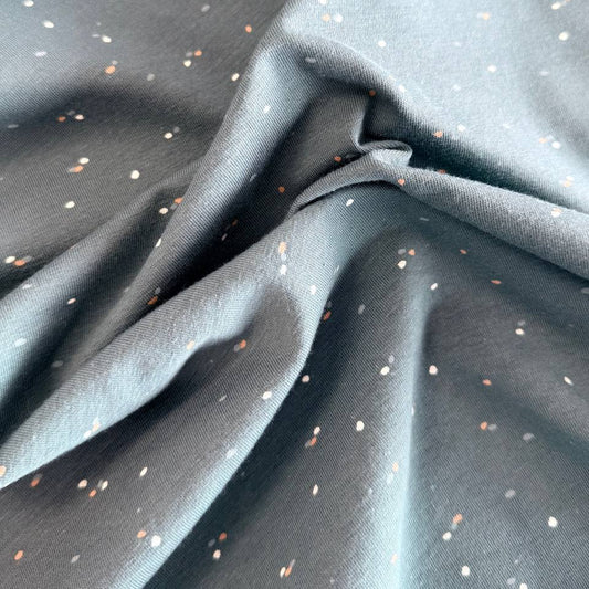 Dusty blue cotton jersey fabric with multicolor speckles, soft stretch knit textile close-up