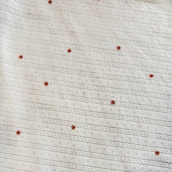 White cotton pointelle knit fabric with small floral print and delicate texture