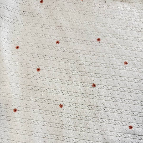 White cotton pointelle knit fabric with small floral print and delicate texture