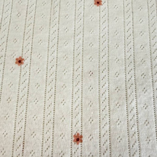 White cotton pointelle knit fabric with small floral print and delicate texture