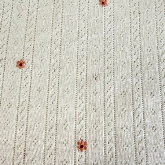 White cotton pointelle knit fabric with small floral print and delicate texture