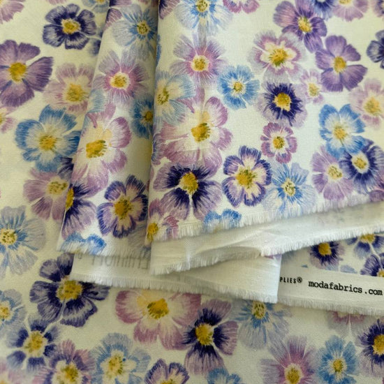 Scattered pastel floral cotton fabric with purple blue and pink flowers on cream background
