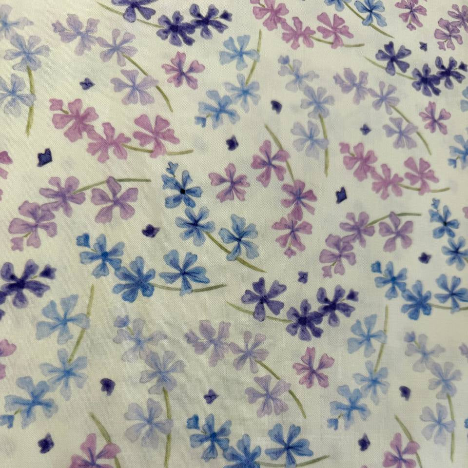 Scattered pastel floral cotton fabric with purple blue and pink flowers on soft cream background
