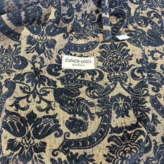 Black and beige woven upholstery fabric with an elegant floral ornamental pattern, used for handmade Sasha’s Atelier bags, cushions, upholstery, and home décor.
