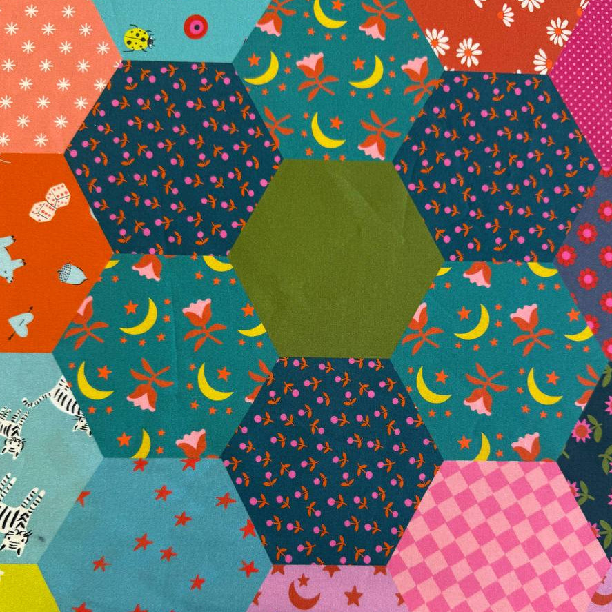 Colorful Ruby Star Society Catnap wide backing fabric with bright hexagon patchwork print featuring florals, stars, moons, and playful animal motifs.