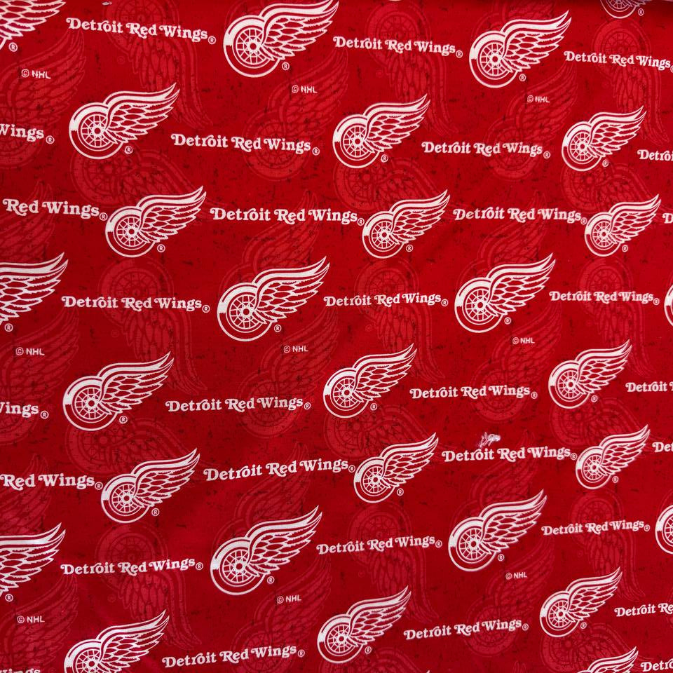 Licensed Detroit Red Wings NHL cotton fabric featuring repeating team logos and hockey-themed print on cotton fabric.
