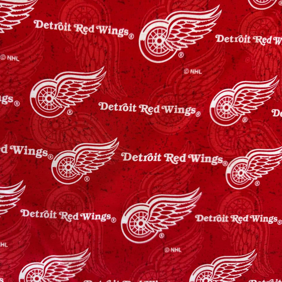 Licensed Detroit Red Wings NHL cotton fabric featuring repeating team logos and hockey-themed print on cotton fabric.