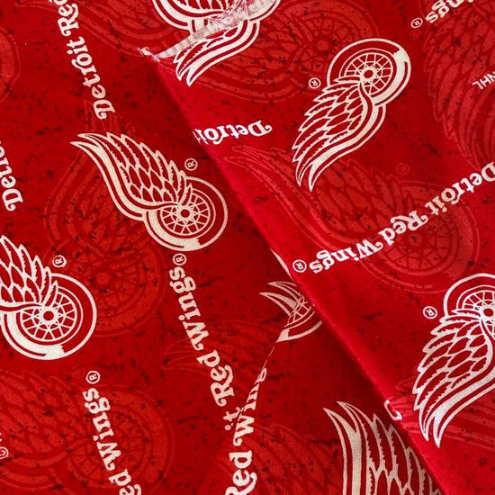 Licensed Detroit Red Wings NHL cotton fabric featuring repeating team logos and hockey-themed print on cotton fabric.