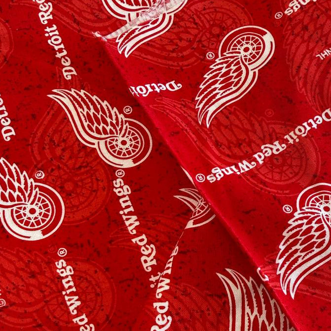 Licensed Detroit Red Wings NHL cotton fabric featuring repeating team logos and hockey-themed print on cotton fabric.