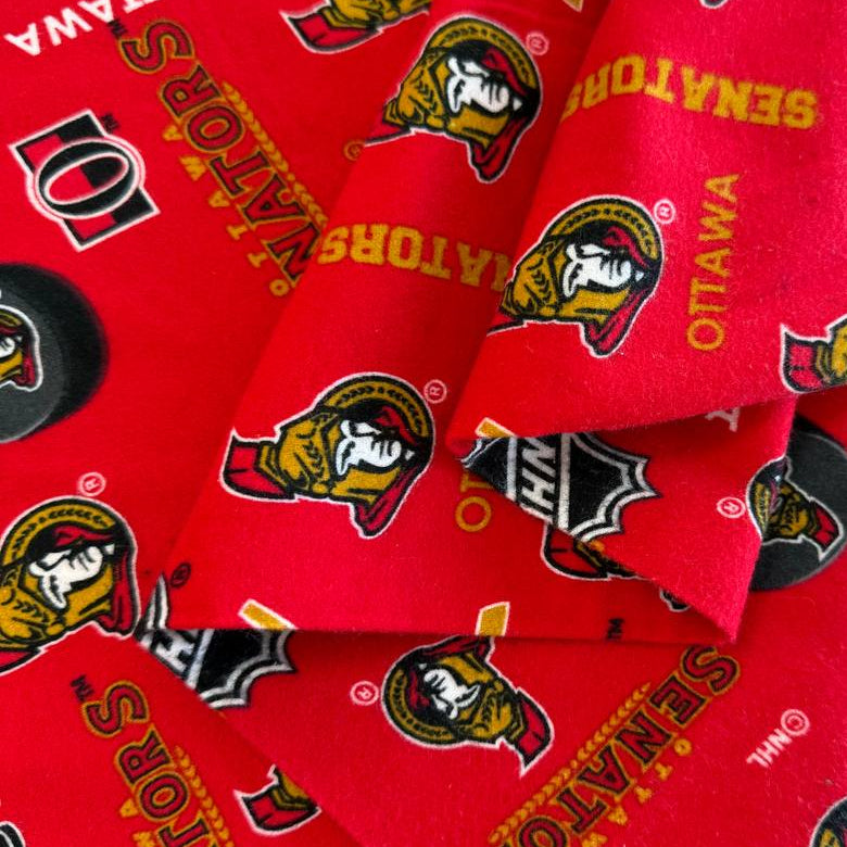 Ottawa Senators NHL cotton flannel fabric with hockey logos, pucks, and sticks on a bright background.