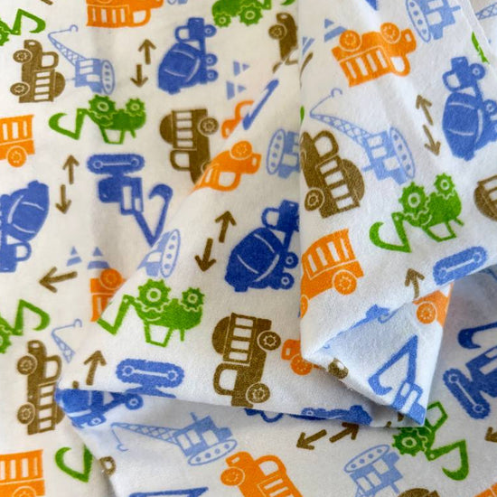 White flannelette fabric featuring colorful construction vehicles including dump trucks, excavators, cranes, and cement mixers in blue, orange, green, and brown.