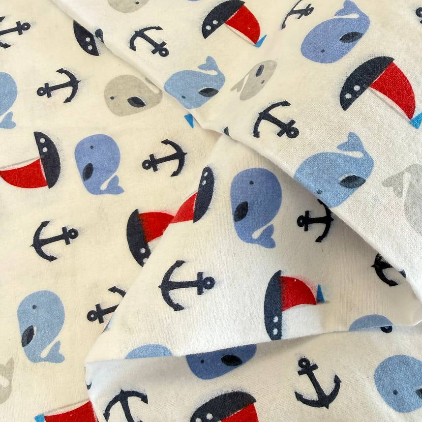 White flannelette fabric featuring blue and grey whales, red sailboats, and navy anchors in a playful nautical pattern.
