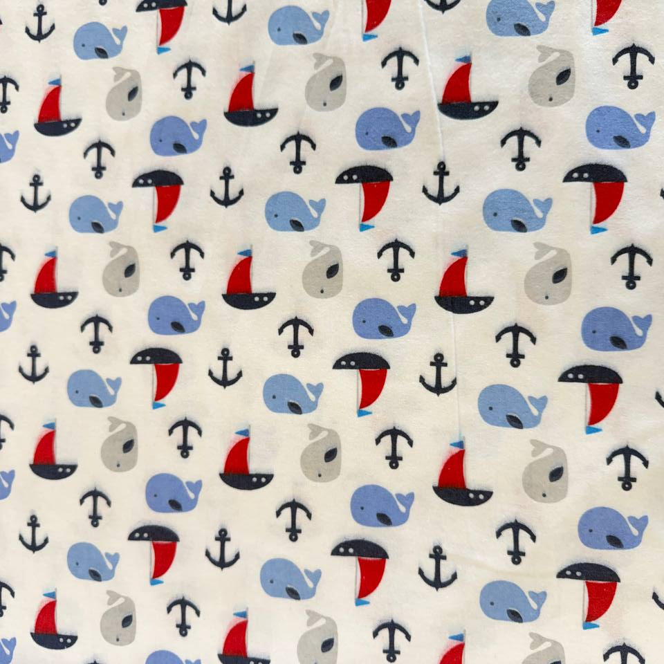 White flannelette fabric featuring blue and grey whales, red sailboats, and navy anchors in a playful nautical pattern.