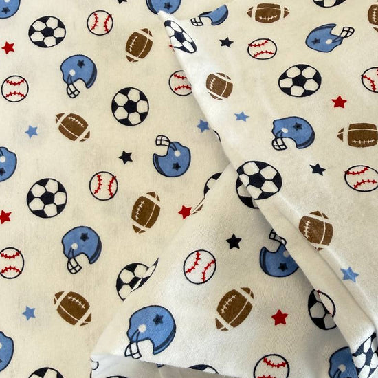 White flannelette fabric featuring soccer balls, baseballs, footballs, blue helmets, and stars in a playful sports-themed pattern.