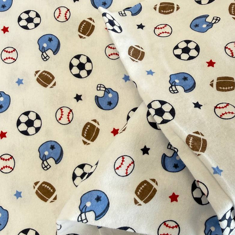 White flannelette fabric featuring soccer balls, baseballs, footballs, blue helmets, and stars in a playful sports-themed pattern.