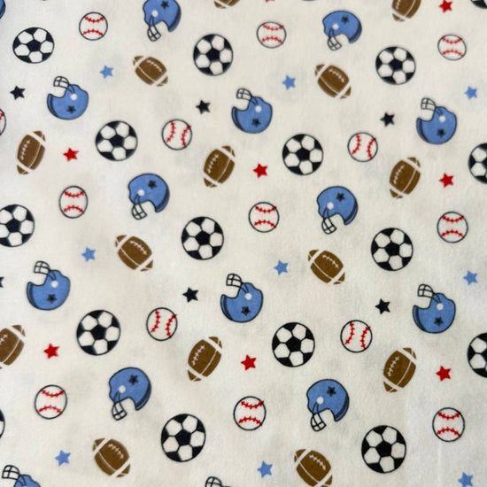 White flannelette fabric featuring soccer balls, baseballs, footballs, blue helmets, and stars in a playful sports-themed pattern.