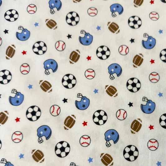 White flannelette fabric featuring soccer balls, baseballs, footballs, blue helmets, and stars in a playful sports-themed pattern.