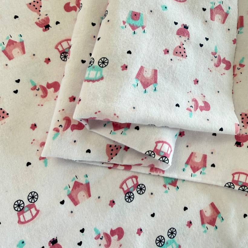 Soft white flannelette fabric featuring pink princesses, unicorns, castles, carriages, dresses, and crowns in a whimsical fairytale print.