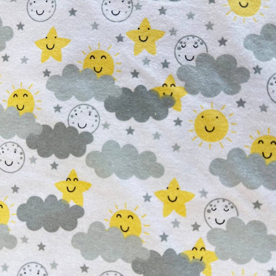 Soft white flannelette fabric featuring smiling yellow suns, stars, moons, and grey clouds in a playful celestial pattern.