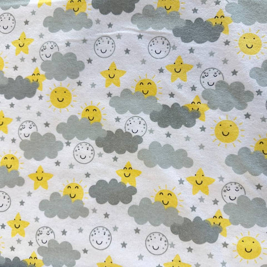 Soft white flannelette fabric featuring smiling yellow suns, stars, moons, and grey clouds in a playful celestial pattern.