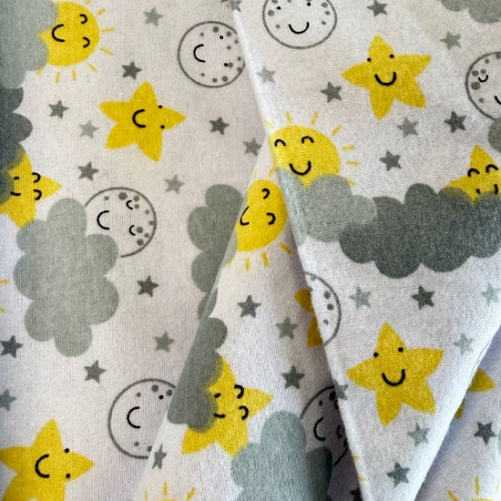 Soft white flannelette fabric featuring smiling yellow suns, stars, moons, and grey clouds in a playful celestial pattern.