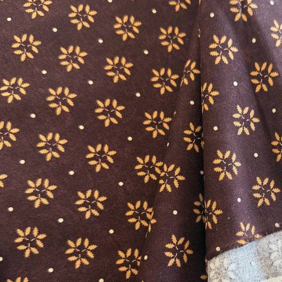 Wheatland quilting cotton fabric by Kansas Troubles Quilters for Moda Fabrics featuring a small repeating floral motif in warm beige tones on a rich mulberry background.