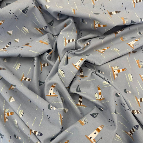 Dusty blue cotton jersey knit fabric with nautical boats, lighthouses and seaside print