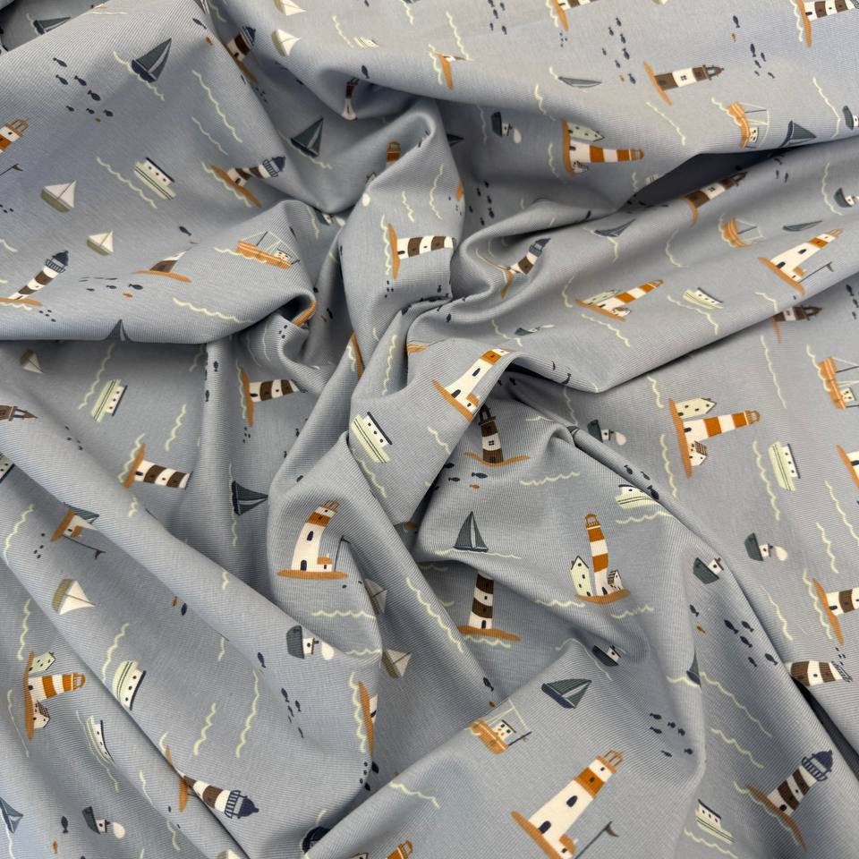 Dusty blue cotton jersey knit fabric with nautical boats, lighthouses and seaside print