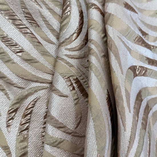 Shiny jacquard fabric in sand, champagne and gold tones featuring a textured abstract leaf pattern with metallic accents.